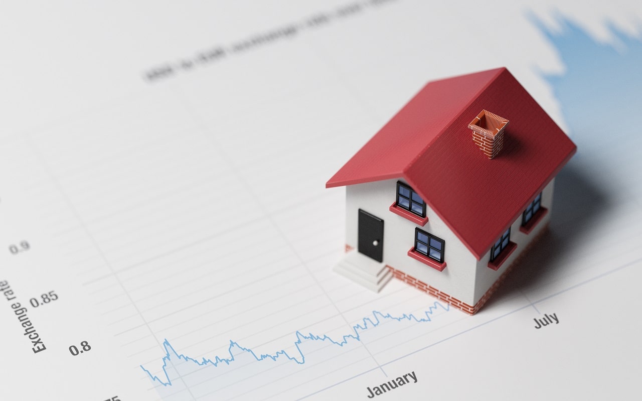 A small model of a red-roofed house placed on a graph depicting exchange rates, illustrating the concept of real estate market analysis.