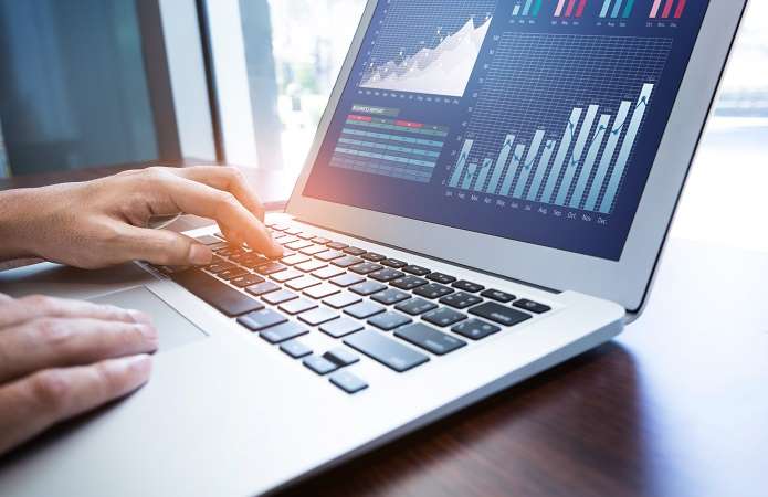  Close-up of a person's hands typing on a laptop keyboard with financial graphs and data analysis displayed on the screen.