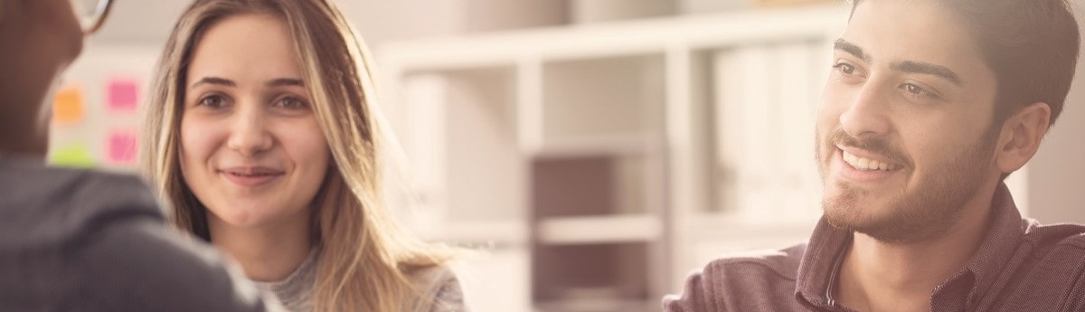 A close-up, blurred image of a young woman and a man smiling at each other in a friendly, professional meeting or negotiation, suggesting a positive interaction in a corporate or business setting.