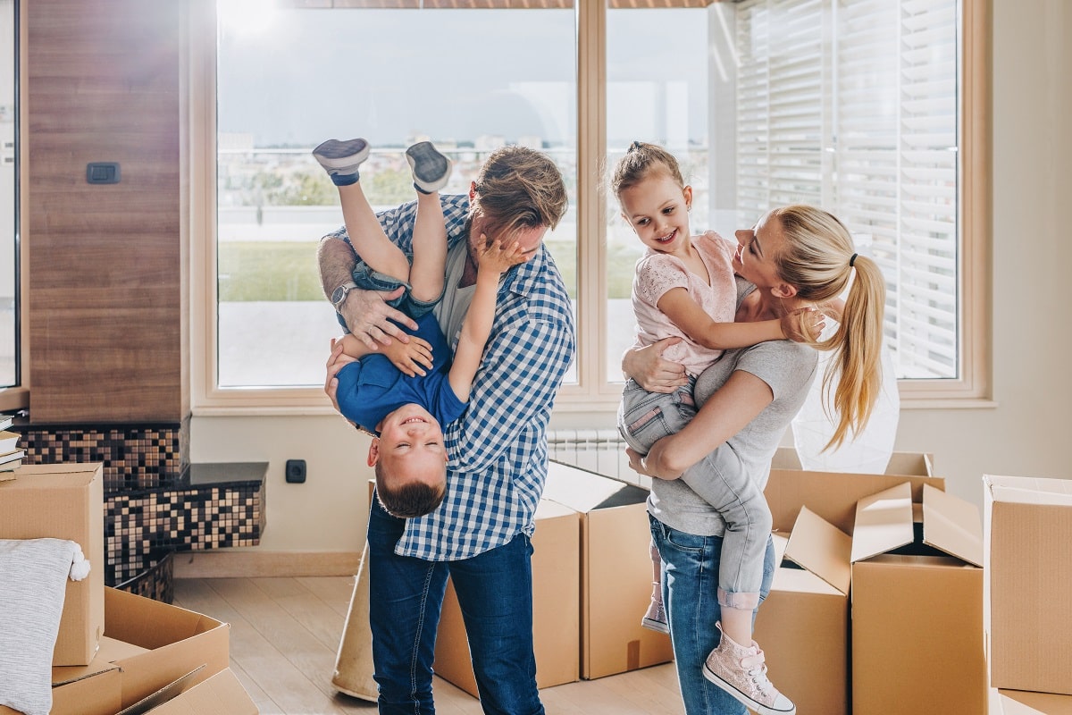 A happy family with two adults and two children playing amidst unpacked boxes, suggesting they are moving into a new home.