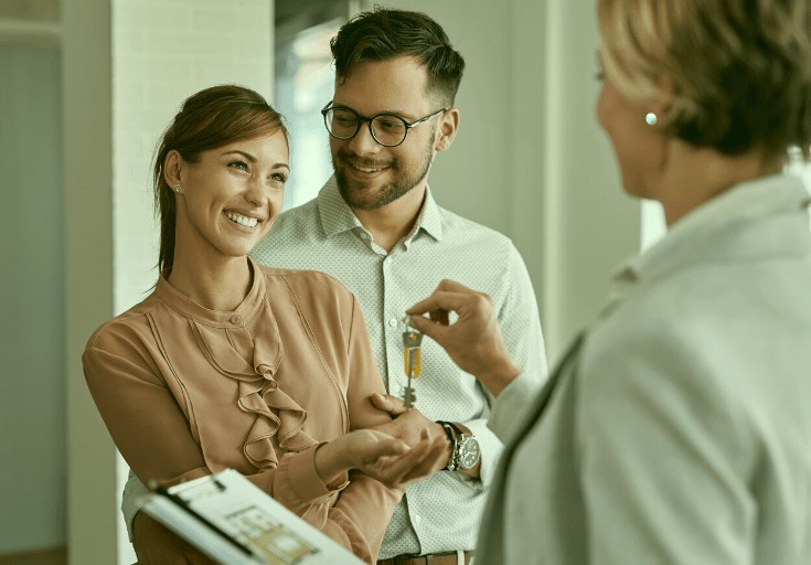 A smiling couple receiving keys from a real estate agent, indicating a new home purchase.